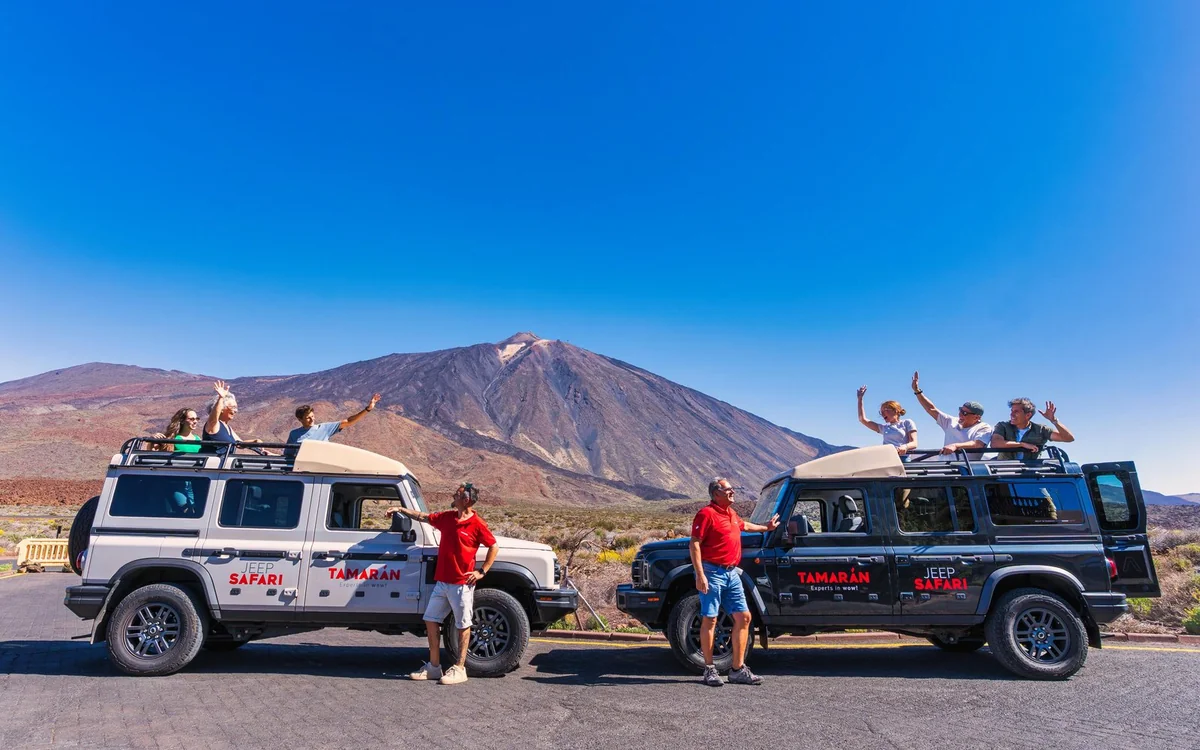 White off-road jeeps parked on gravel with people in red jackets standing beside them