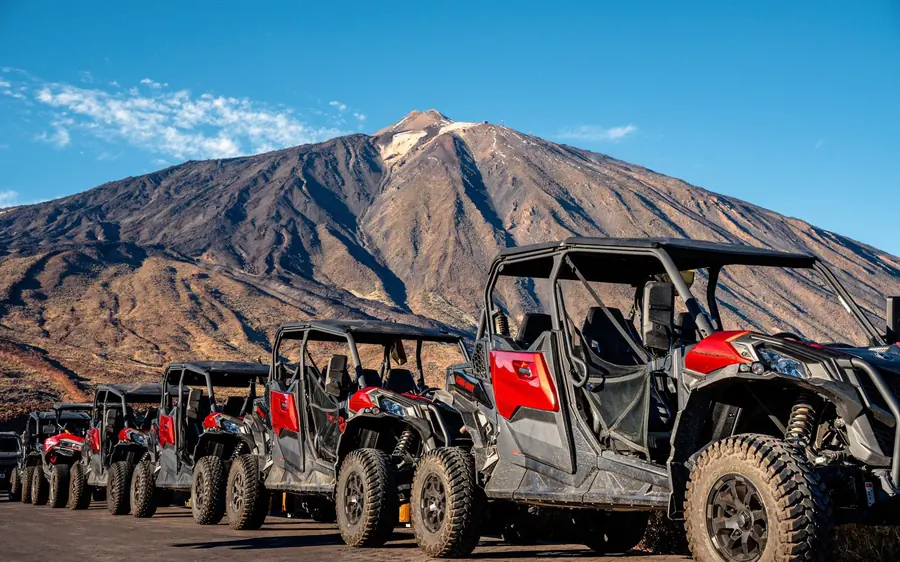 A row of red and black buggies parked on gravel below the mountain