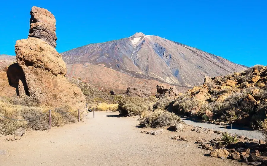 A tall rock pillar standing in front of the Teide cone under a blue sky