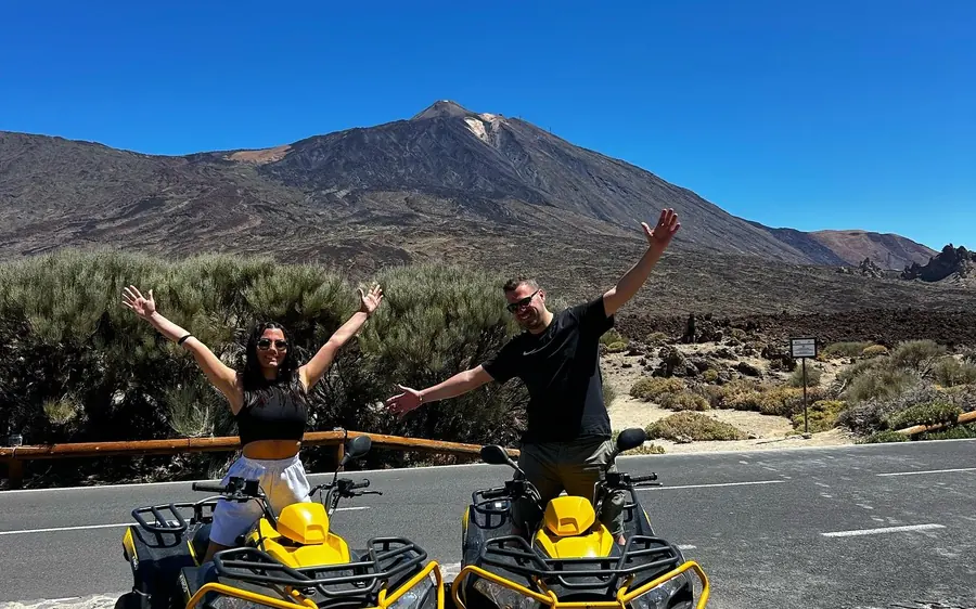 Two riders on quads with their arms raised on a park road