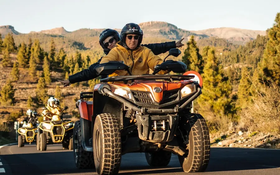 A line of quads with riders on a park road, the Teide cone behind them