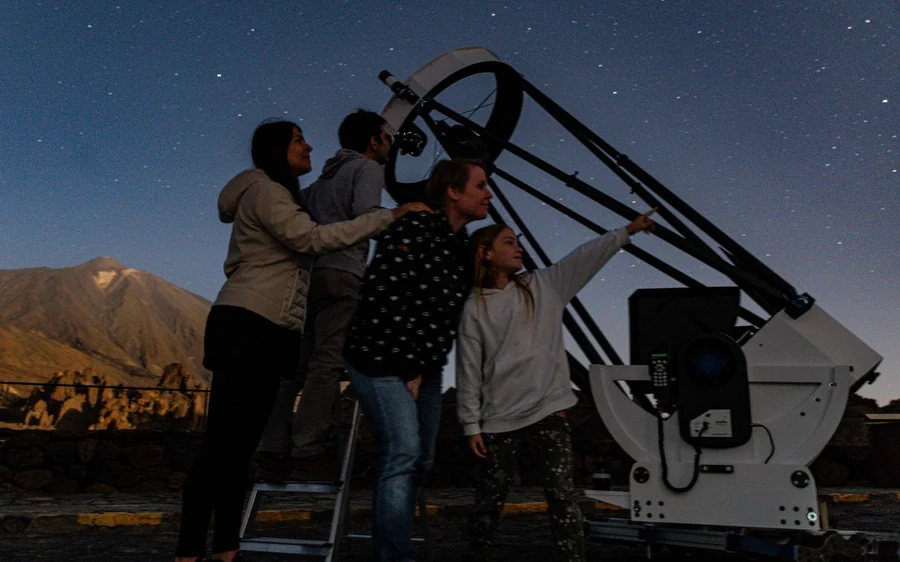 A group gathered around a large telescope at dusk