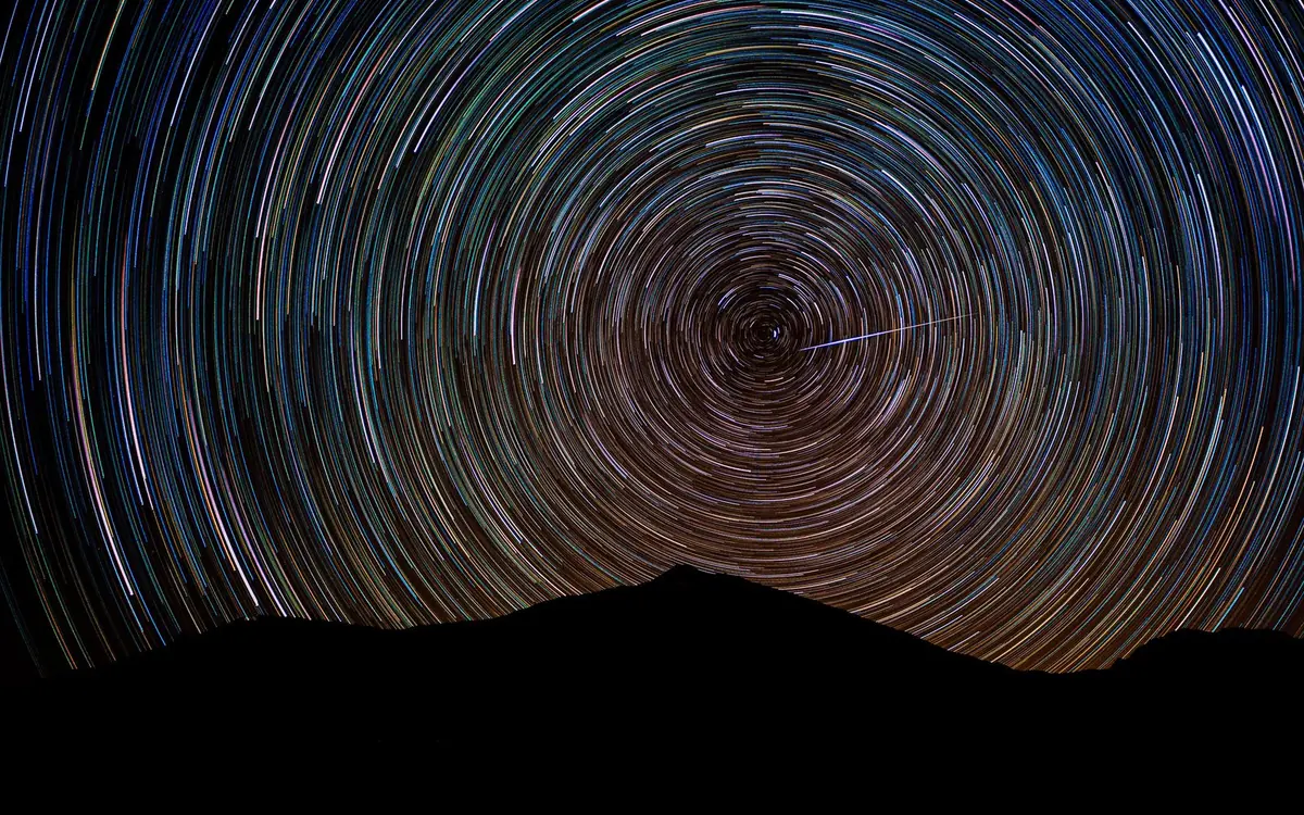 Circular star trails traced across a dark sky above a black ridge