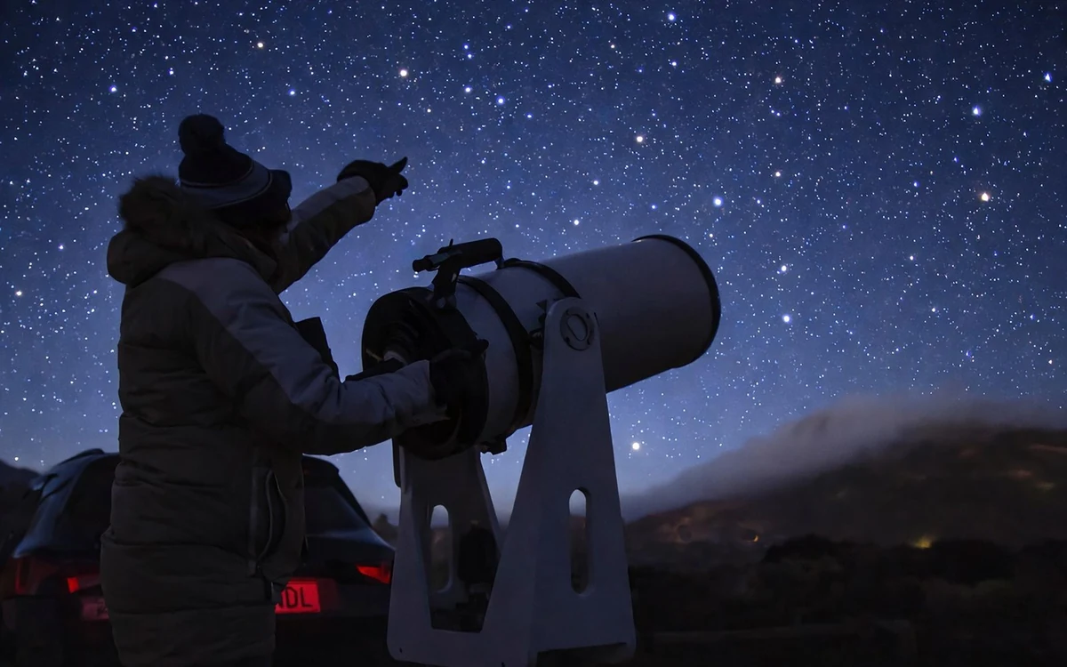 A guide standing beside a large telescope under a star-filled sky
